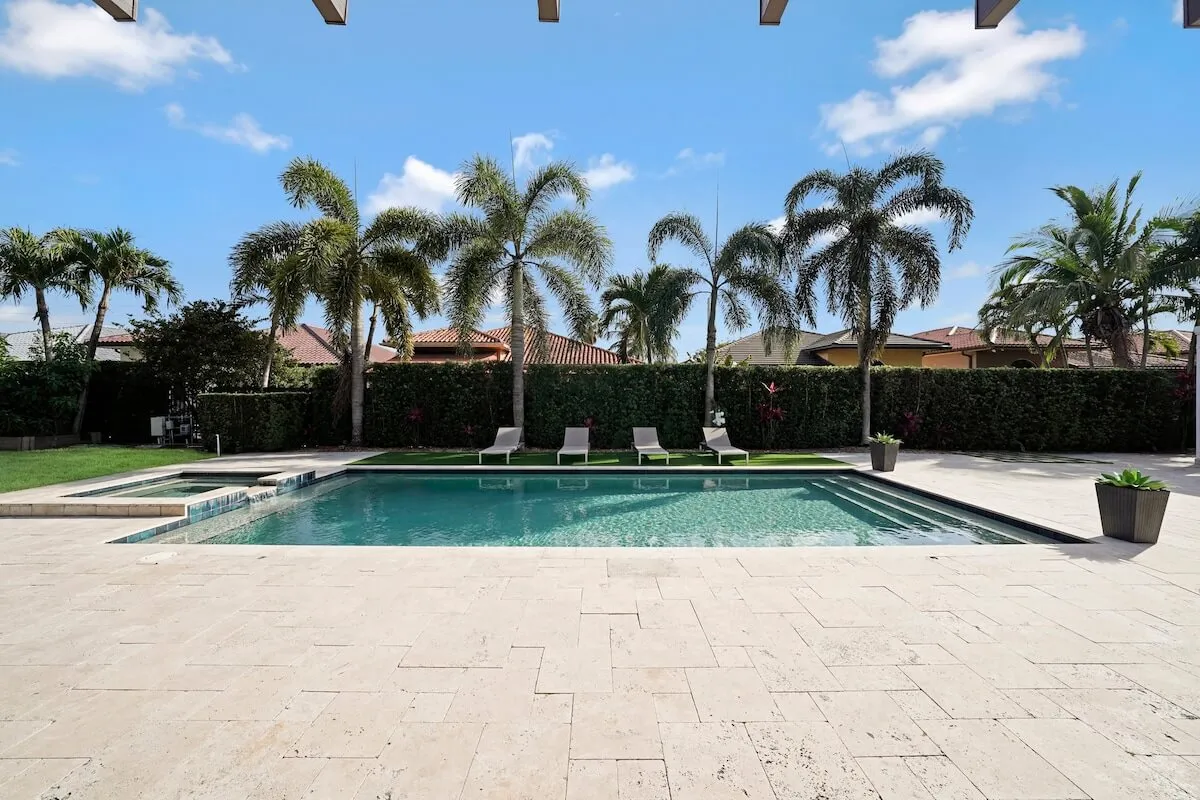 A tranquil swimming pool surrounded by lounge chairs, palm trees, and a garden area. The setting is perfect for both relaxation and play, with ample space for children to splash in the water while adults unwind nearby. The scene is inviting and family-friendly, capturing the quintessential resort-style backyard.