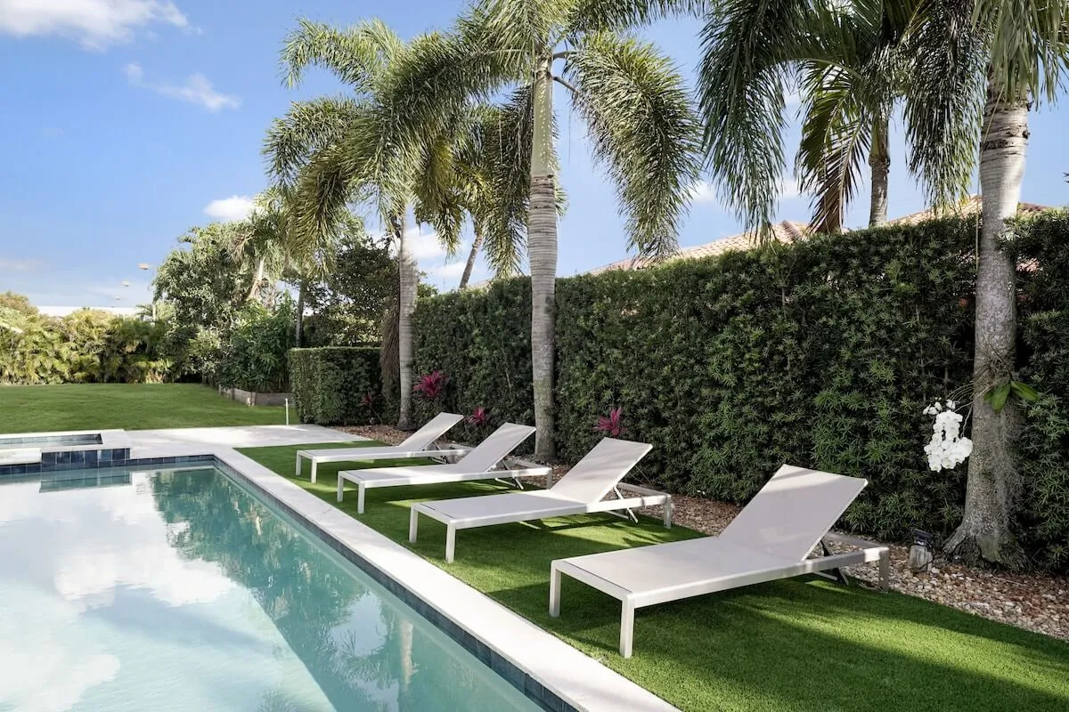 The serene backyard showcases a sparkling swimming pool surrounded by lounge chairs and palm trees. The tranquil atmosphere hints at relaxation and outdoor leisure, ideal for unwinding after work or entertaining colleagues and friends.
